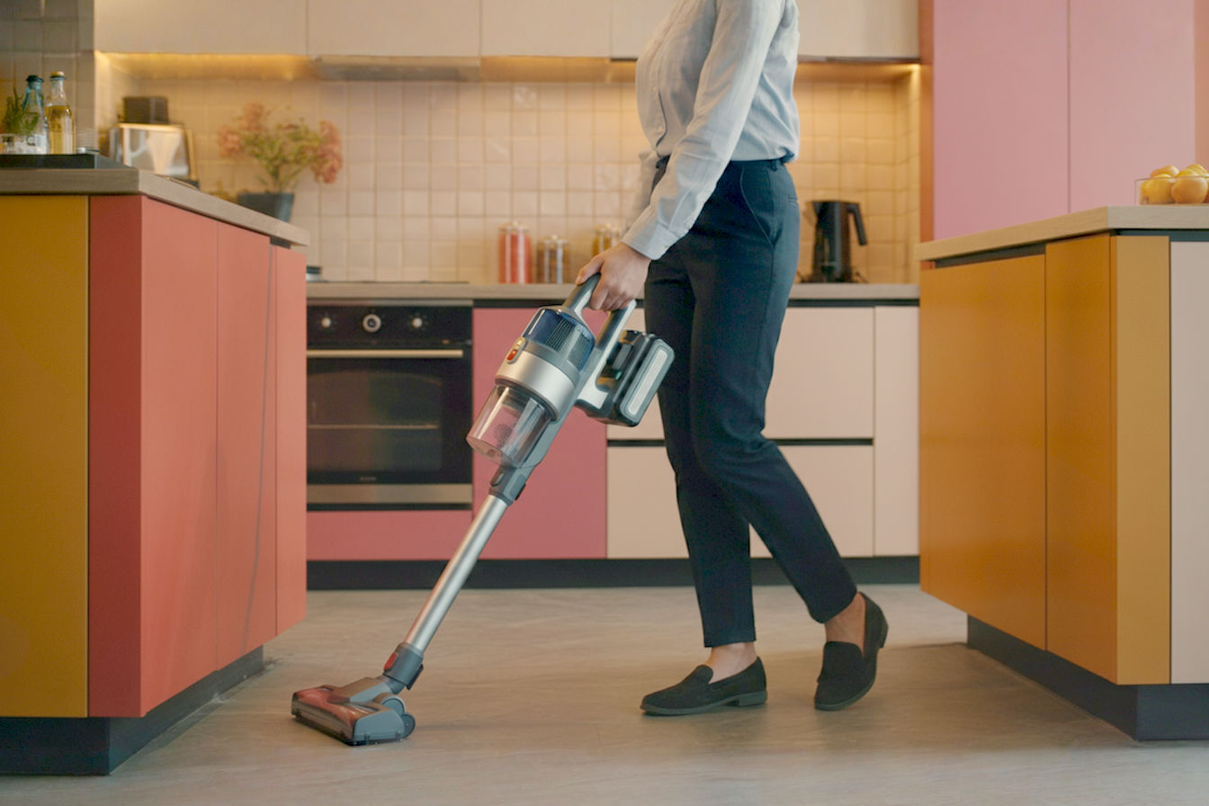 Professional cleaning staff member using a sleek, modern cordless commercial vacuum in a well-lit hotel lobby. The image should capture the freedom of movement without cords, showing the vacuum's ergonomic design and the cleaner's ease of operation. Soft natural lighting highlights the vacuum's features while conveying a sense of cleanliness and efficiency.